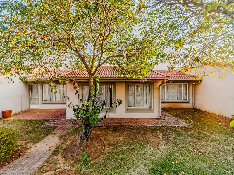 Rear view of a townhouse featuring a terracotta tiled roof, brick paved patio area, and established garden with mature trees.