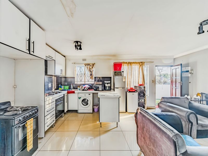 Open-plan kitchen and living area featuring tiled floors, built-in cabinetry, and direct access to the exterior, showing signs of ceiling water damage.