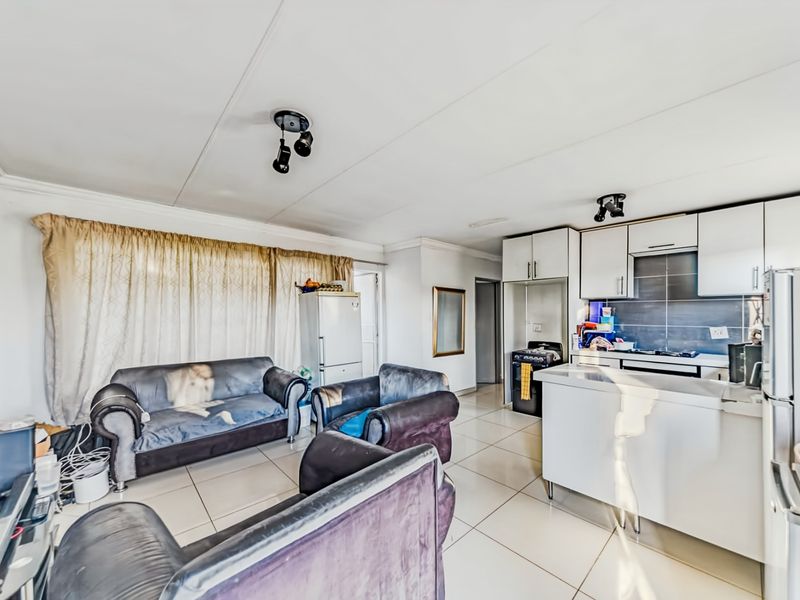 Open-plan living and kitchen area featuring tiled flooring, built-in cabinetry, and a central kitchen island, offering a functional layout for modern living.