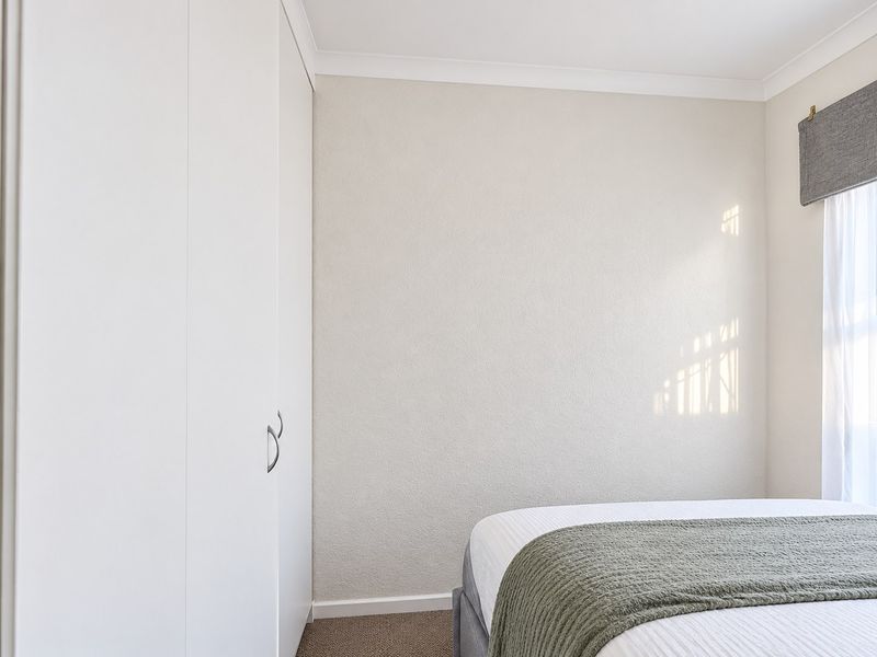 A bright and well-maintained bedroom featuring neutral walls, carpet flooring, and a built-in wardrobe with clean white cabinetry.
