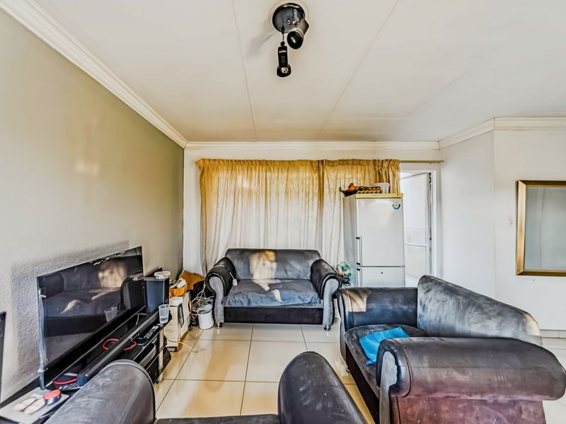 A living room area featuring tiled flooring and ceiling cornice, requiring cosmetic updates to improve the overall aesthetic and condition of the space.