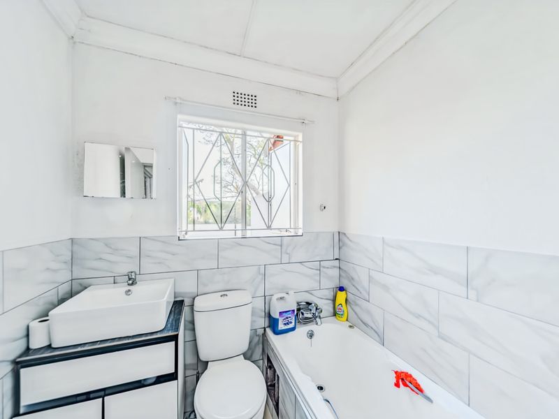 A clean, modern bathroom featuring a vessel sink on a vanity cabinet, a standard toilet, and a bathtub with marble-look wall tiling.
