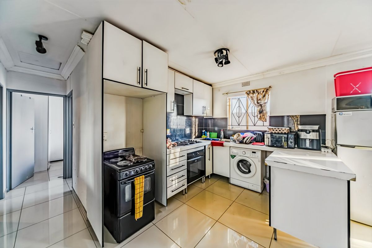A functional kitchen featuring tiled flooring, built-in cabinetry, a gas stove, and an integrated washing machine, offering potential for modernization.