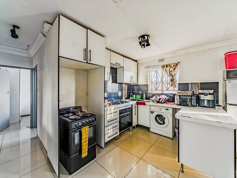A functional kitchen featuring tiled flooring, built-in cabinetry, a gas stove, and an integrated washing machine, offering potential for modernization.
