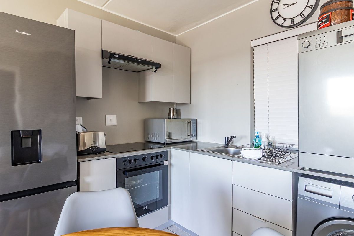 Compact modern kitchen featuring sleek cabinetry, integrated oven and hob, extractor fan, and stainless steel sink with convenient laundry appliance space.