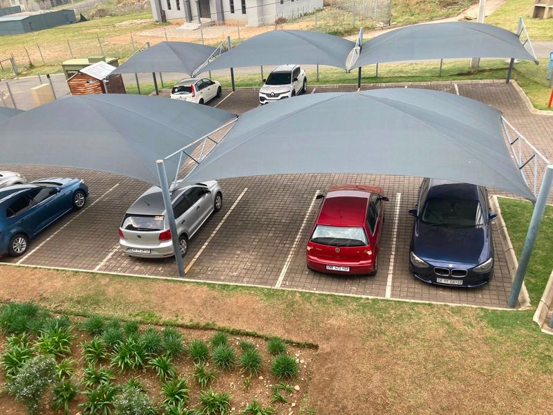 An elevated view of an outdoor parking area featuring multiple paved bays covered by grey shade cloth structures.