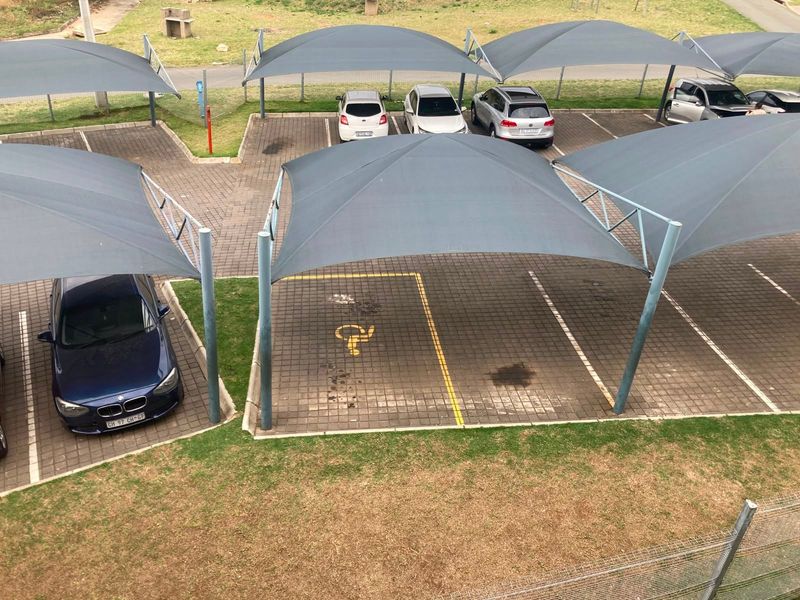 Outdoor parking area featuring multiple paved bays covered by shade cloth structures, including a designated disabled parking space.