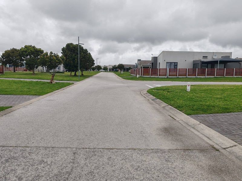 A view of the residential street within the townhouse complex, featuring paved roads, manicured verges, and modern boundary fencing.