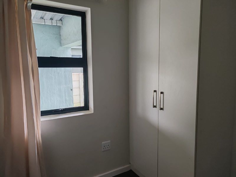 A bedroom featuring a built-in wardrobe, neutral wall finishes, and an aluminium-framed window providing natural light.