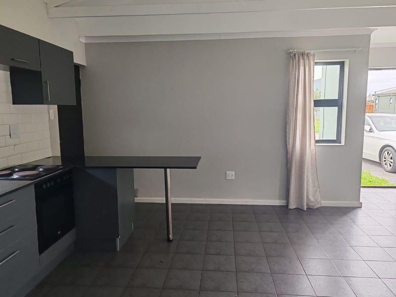 Open plan kitchen and living area featuring dark cabinetry, built-in oven, electric hob, breakfast bar, and tiled flooring with exposed ceiling beams.