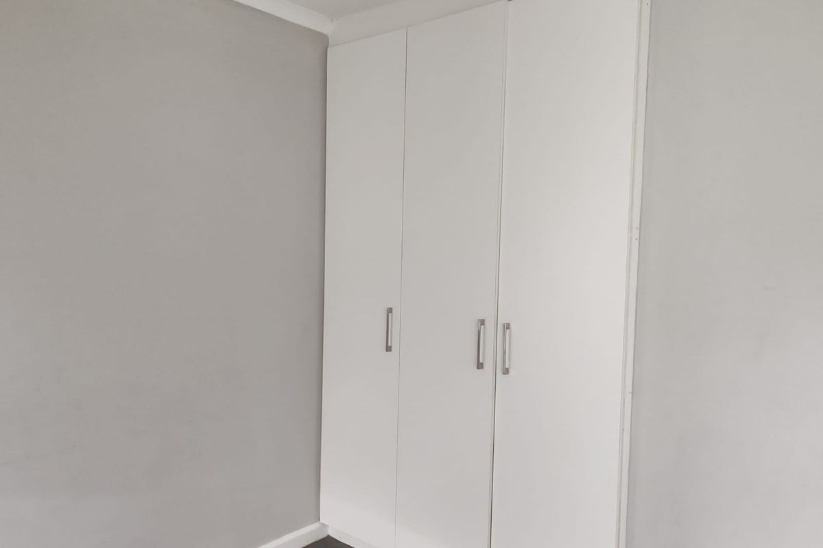 A clean, empty bedroom featuring neutral grey walls, tiled flooring, and white built-in cupboards with modern handles.