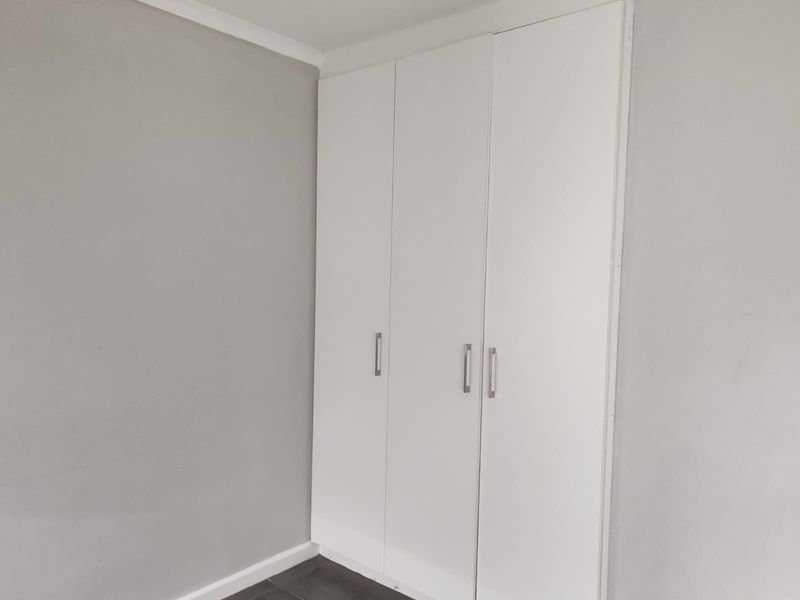 A clean, empty bedroom featuring neutral grey walls, tiled flooring, and white built-in cupboards with modern handles.