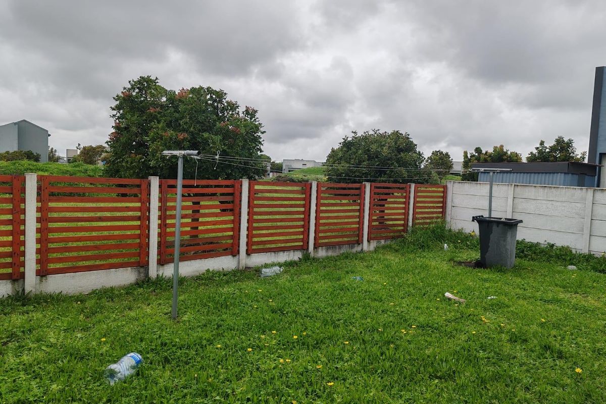 A rear garden area featuring a timber slat fence, concrete boundary wall, and a rotary clothesline set within a grassed yard.