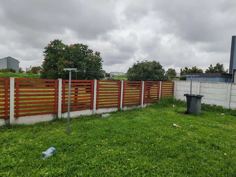 A rear garden area featuring a timber slat fence, concrete boundary wall, and a rotary clothesline set within a grassed yard.