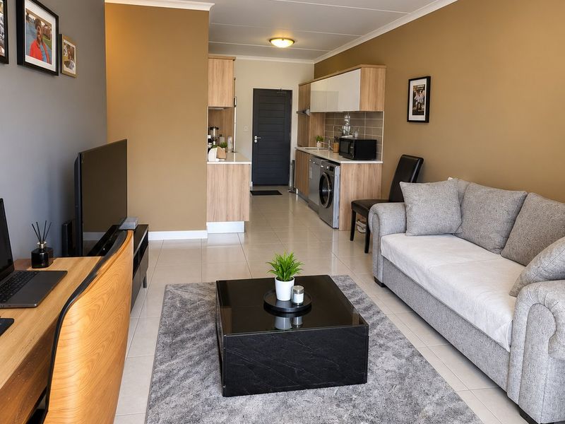 An open-plan living and kitchen area featuring tiled flooring, modern cabinetry, and integrated laundry appliances, creating a functional and cohesive living space.