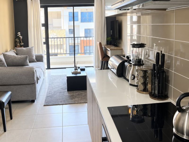 Modern open-plan apartment featuring a sleek kitchen with built-in appliances and tiled flooring, seamlessly flowing into a living area with balcony access.