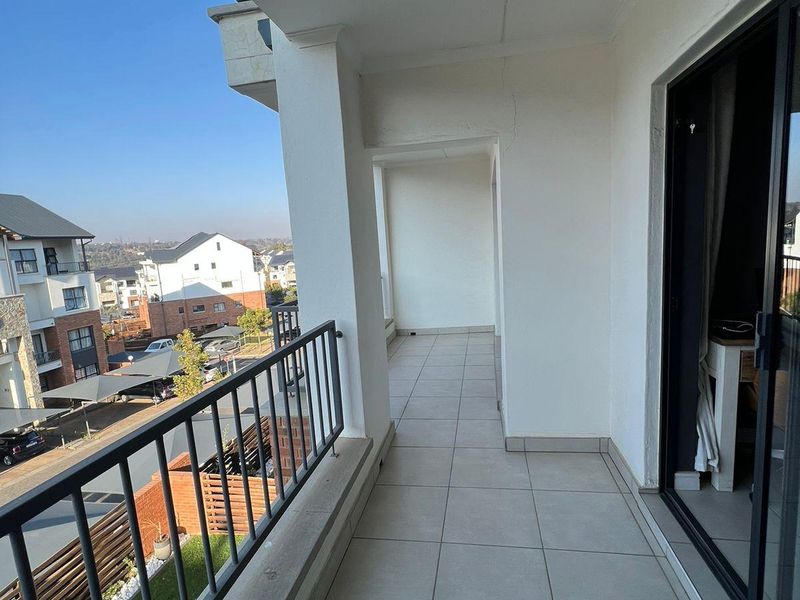 A spacious covered balcony featuring tiled flooring, a metal balustrade, and sliding glass door access, offering an elevated view of the surrounding residential complex.