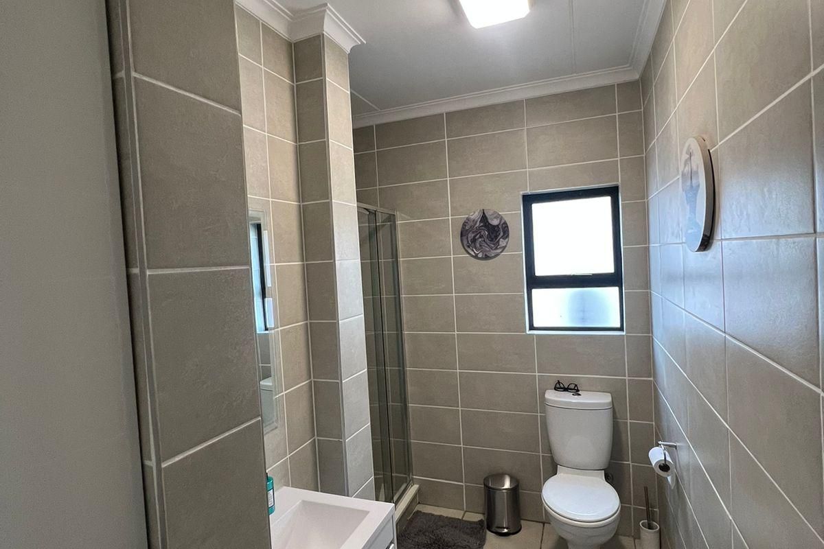 A functional bathroom featuring a shower enclosure, vanity basin, and toilet, finished with neutral wall and floor tiles.