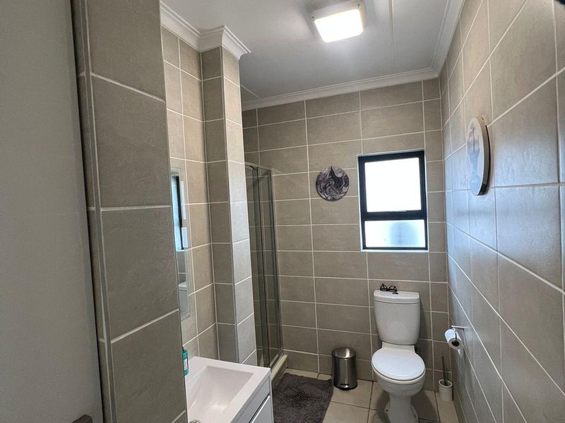 A functional bathroom featuring a shower enclosure, vanity basin, and toilet, finished with neutral wall and floor tiles.