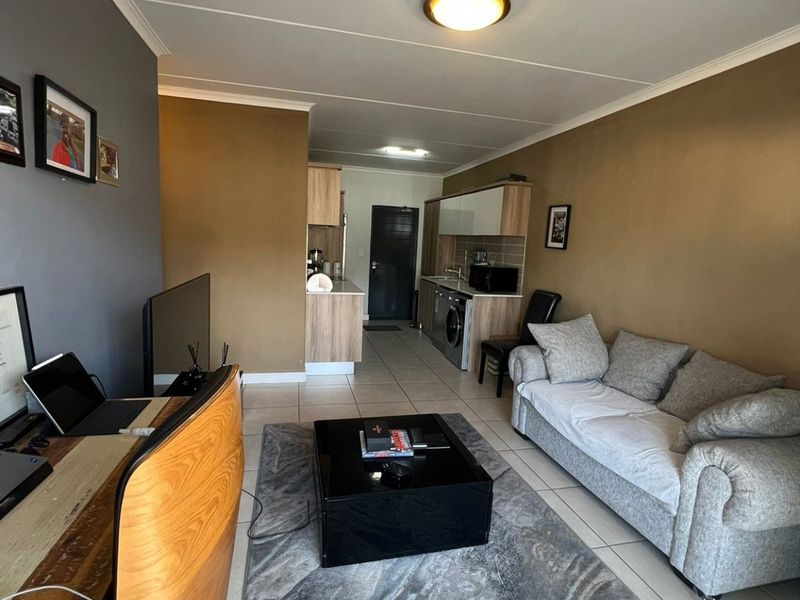 Open-plan living area featuring tiled floors and a compact kitchen with built-in cabinetry and laundry plumbing.