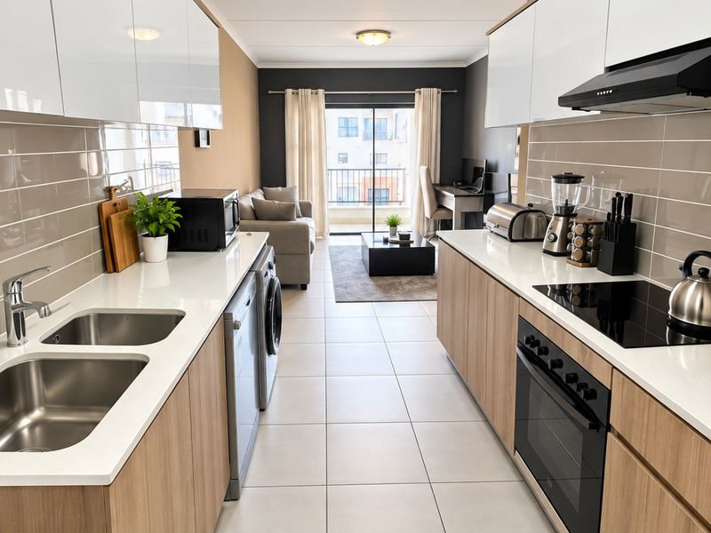 Modern open-plan kitchen featuring sleek cabinetry, stone countertops, integrated appliances, and tiled flooring, flowing seamlessly into the living area with balcony access.