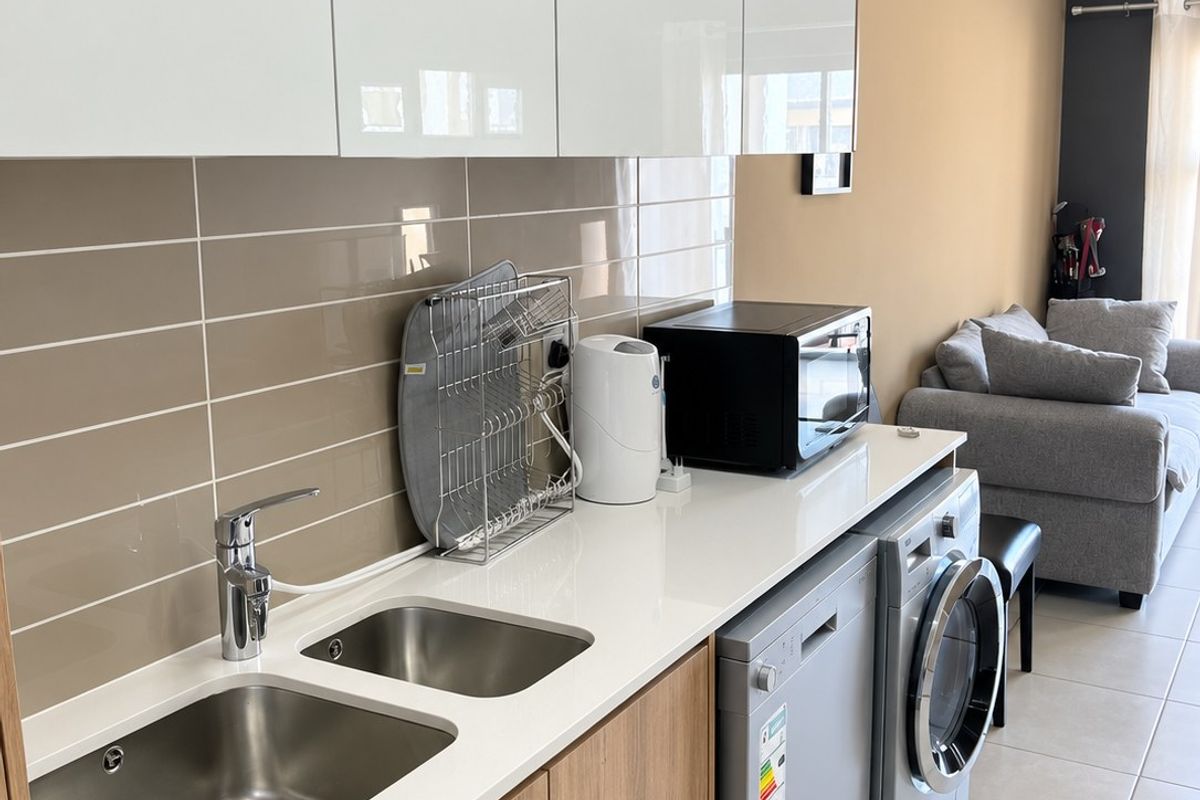 Modern kitchen area featuring sleek white cabinetry, wood-finish lower cupboards, quartz countertops, and a double stainless steel sink with tiled backsplash.