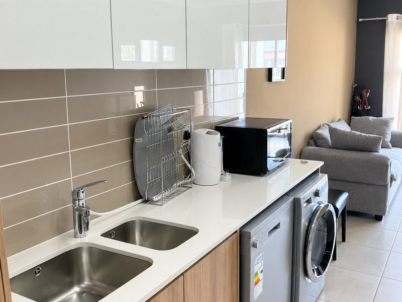 Modern kitchen area featuring sleek white cabinetry, wood-finish lower cupboards, quartz countertops, and a double stainless steel sink with tiled backsplash.