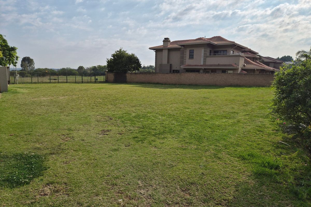 A spacious, well-maintained residential plot featuring a manicured lawn, perimeter wall, and secure metal fencing.