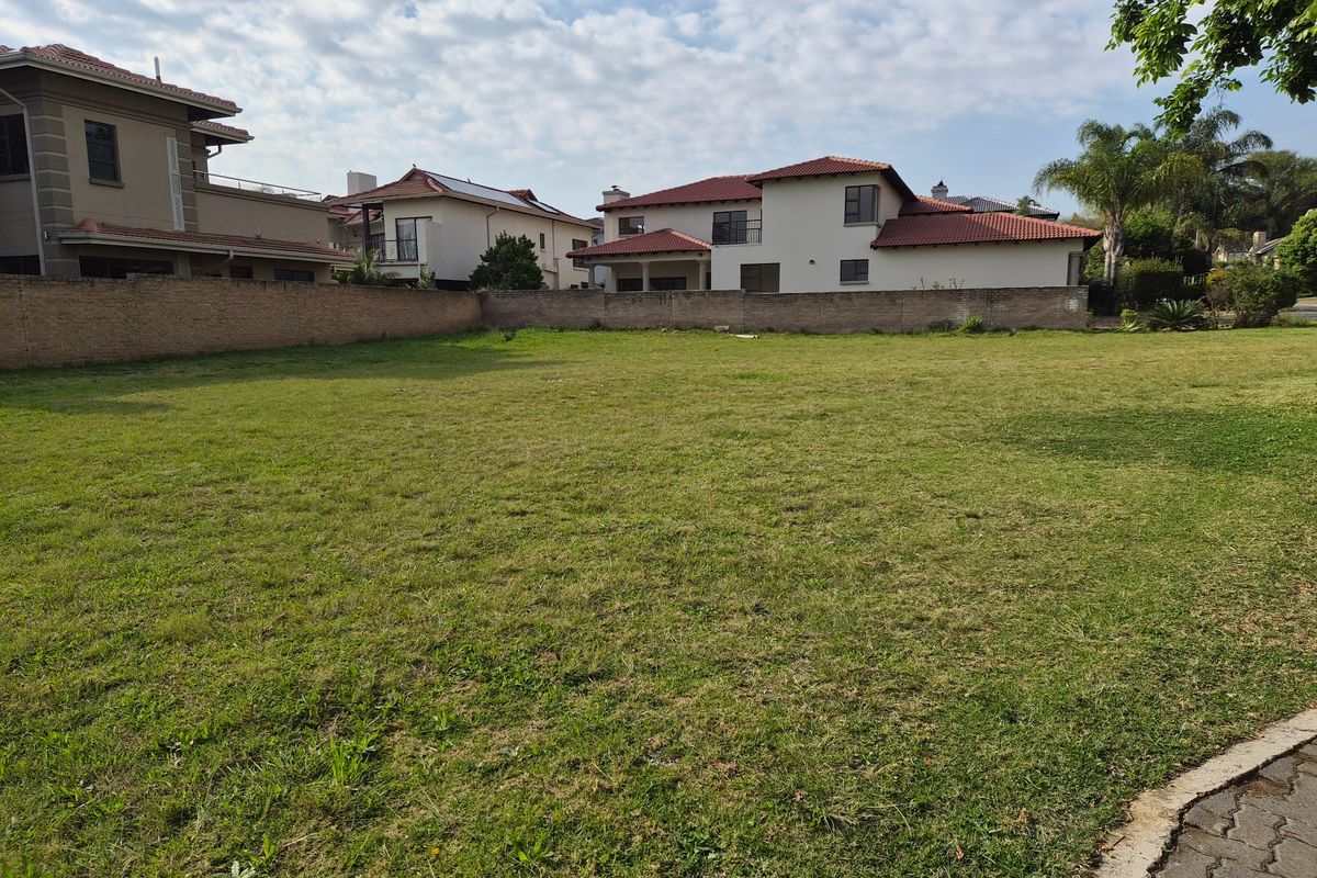 A vacant residential plot featuring a level grassed area enclosed by a perimeter wall, situated within an established residential neighborhood.