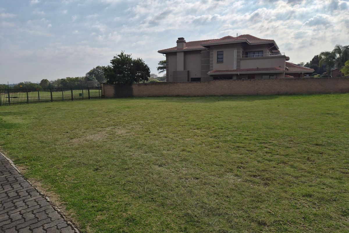 A spacious vacant residential plot featuring a well-maintained grass lawn, enclosed by a brick boundary wall and perimeter fencing.