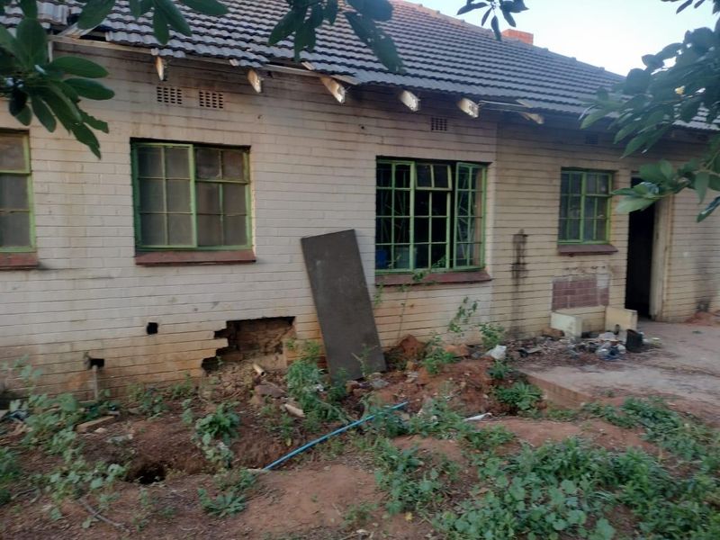 Rear exterior view of a house showing significant structural damage to the roofline and brickwork, requiring extensive maintenance and repair.