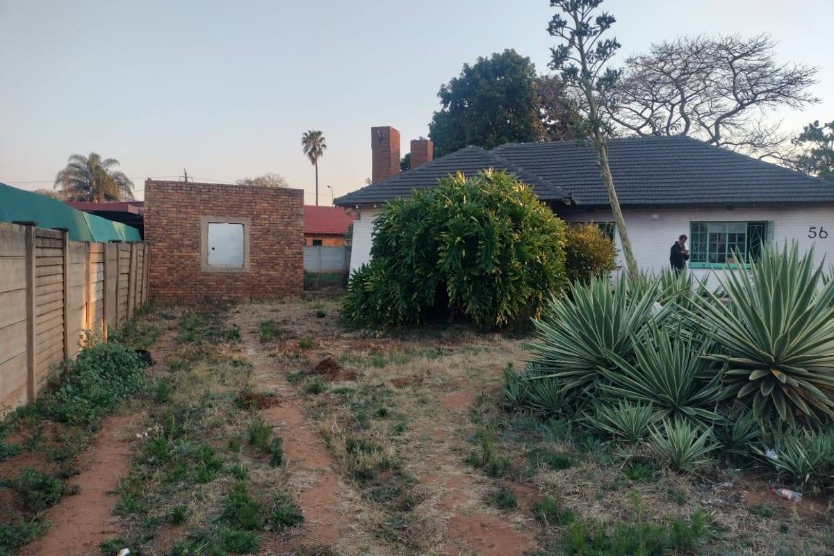 Rear view of the property featuring a tiled roof house, a detached brick outbuilding, and a large, unmaintained garden area.