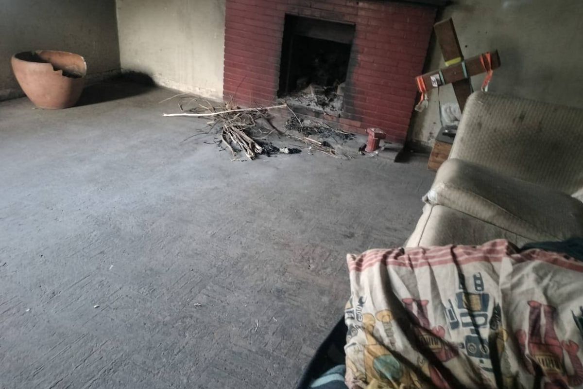 A living room featuring a brick fireplace, showing significant signs of wear and requiring extensive renovation to restore the space.