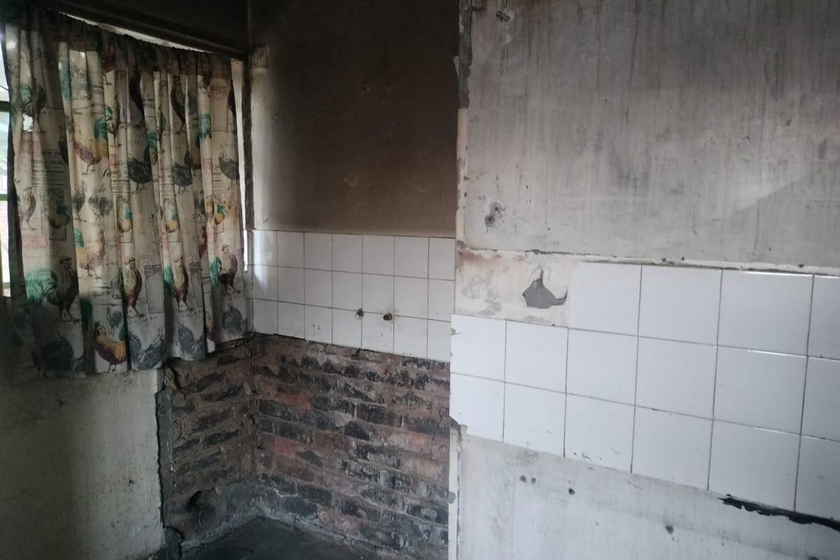 A severely damaged kitchen area requiring complete renovation, featuring exposed brickwork and damaged wall surfaces.