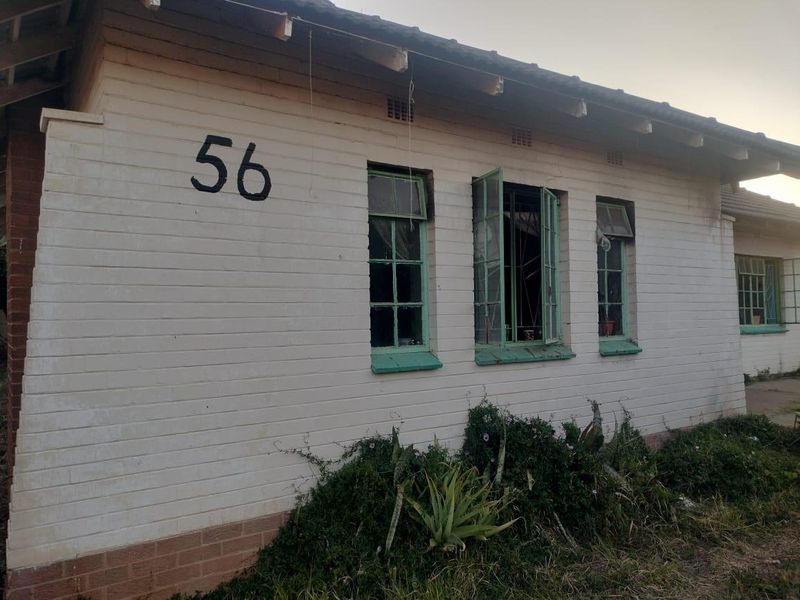 Exterior view of a single-story brick house featuring painted walls, steel-framed windows, and a tiled roof, showing signs of wear and maintenance needs.