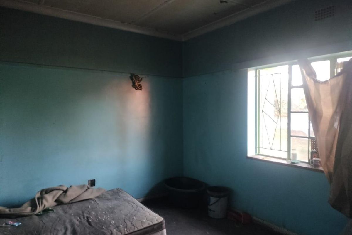 A bedroom featuring a steel window with security gate, requiring significant cosmetic updates and repairs to the walls and ceiling.