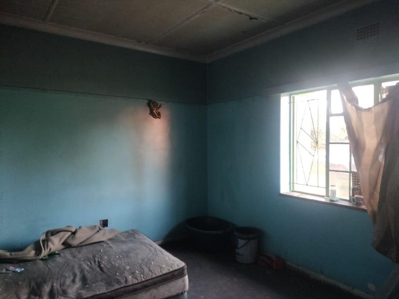 A bedroom featuring a steel window with security gate, requiring significant cosmetic updates and repairs to the walls and ceiling.