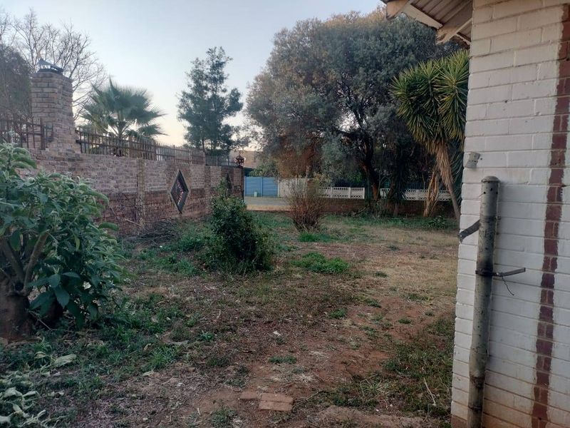 A view of the rear garden area featuring a brick boundary wall, chimney structure, and established trees.