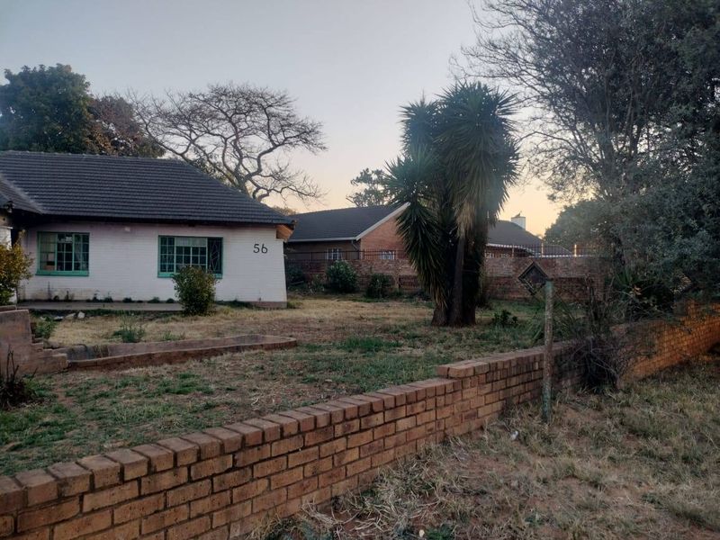 Front view of a single-story house featuring a tiled roof, security bars on windows, and a large front garden with a brick boundary wall.