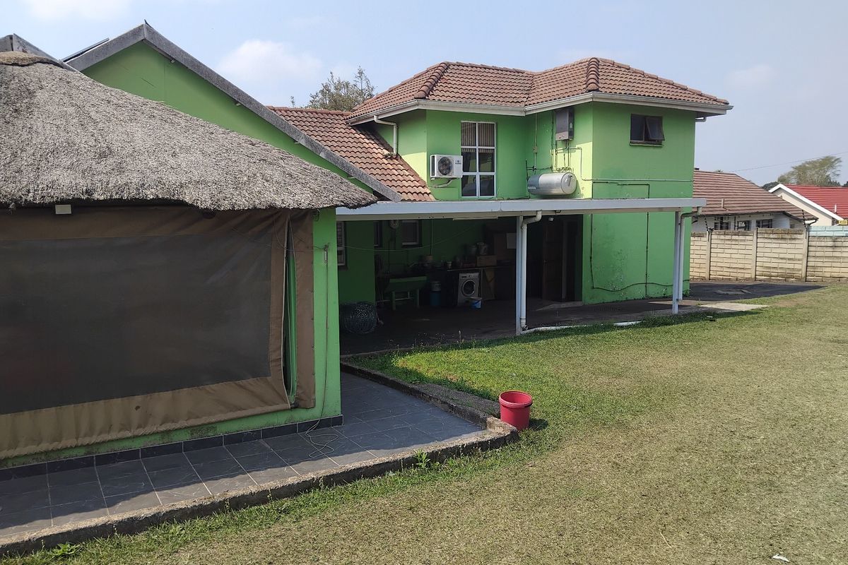 Rear view of a two-story house featuring a thatched-roof patio area, tiled roofing, and a large lawn with boundary walling.