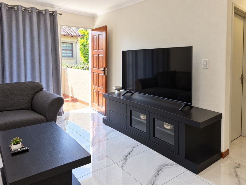 A well-maintained living room featuring polished marble-look floor tiles and direct access to an outdoor balcony through a timber door.