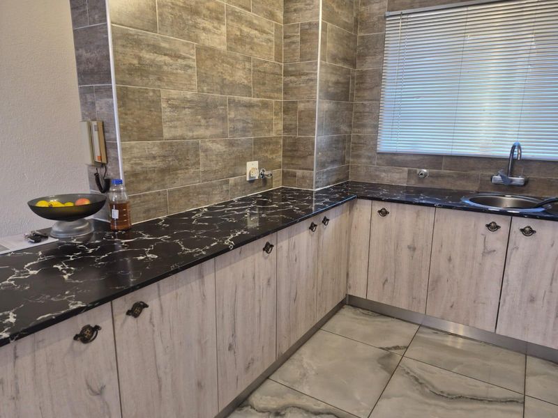 A functional kitchen featuring wood-grain cabinetry, black marble-effect countertops, tiled backsplash, and a stainless steel sink with a mixer tap.