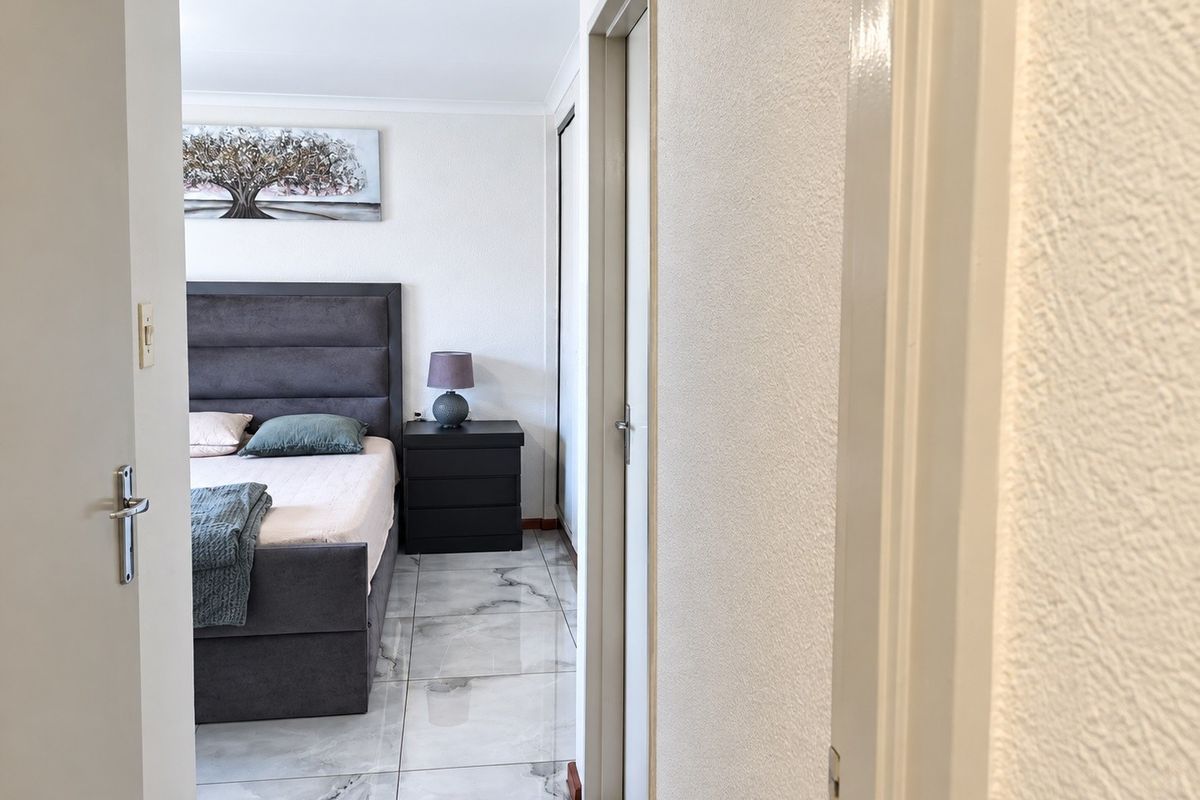 A well-lit bedroom featuring polished marble-look floor tiles and a built-in wardrobe, viewed from the adjacent hallway.