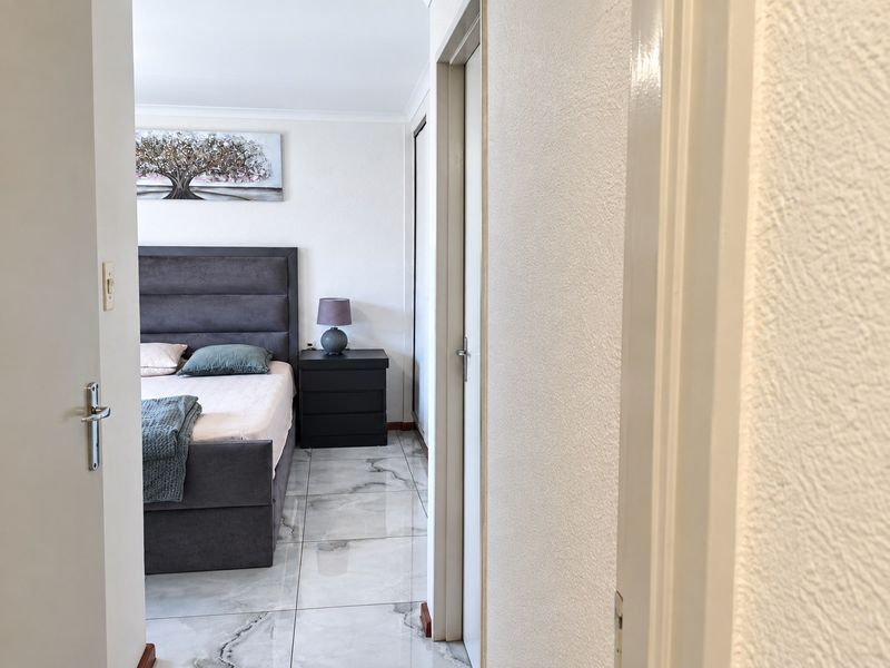 A well-lit bedroom featuring polished marble-look floor tiles and a built-in wardrobe, viewed from the adjacent hallway.