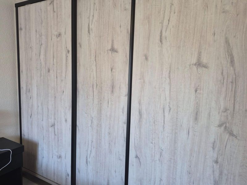 A close-up view of a modern built-in wardrobe with light wood-grain finish and dark trim detailing.