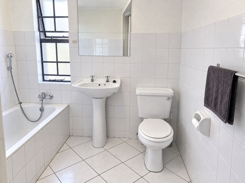 A functional bathroom featuring a pedestal basin, toilet, and bathtub with a handheld shower mixer, finished with white wall and floor tiles.