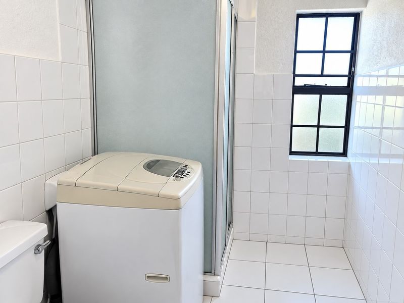 A functional laundry area featuring tiled walls and flooring, a shower enclosure, and a grid-style window providing natural light.