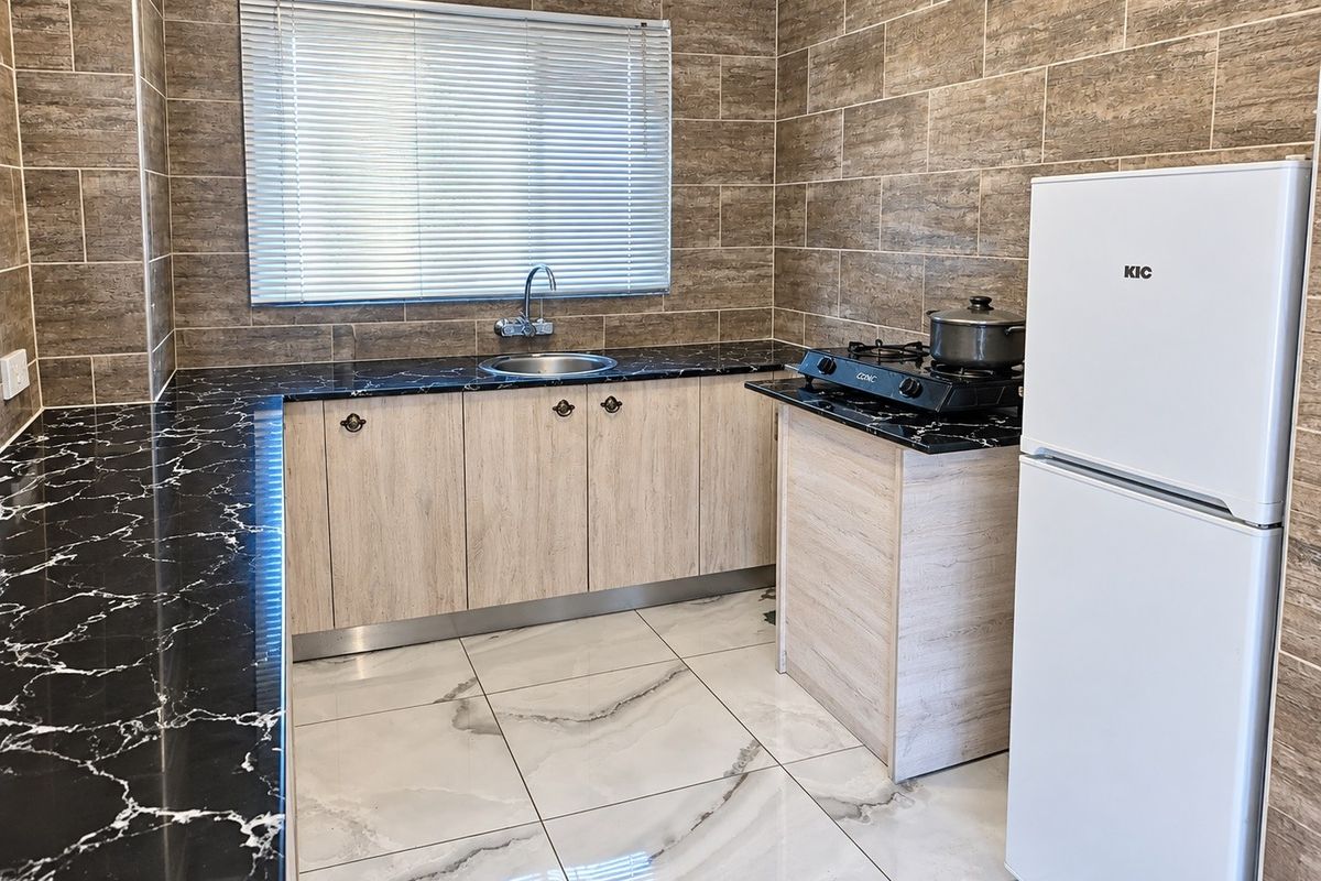 Modern kitchen featuring marble-effect countertops, light wood-finish cabinetry, stainless steel sink, and contemporary tiled walls and flooring.