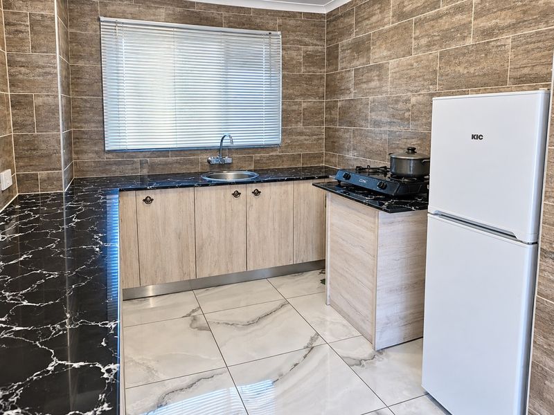 Modern kitchen featuring marble-effect countertops, light wood-finish cabinetry, stainless steel sink, and contemporary tiled walls and flooring.