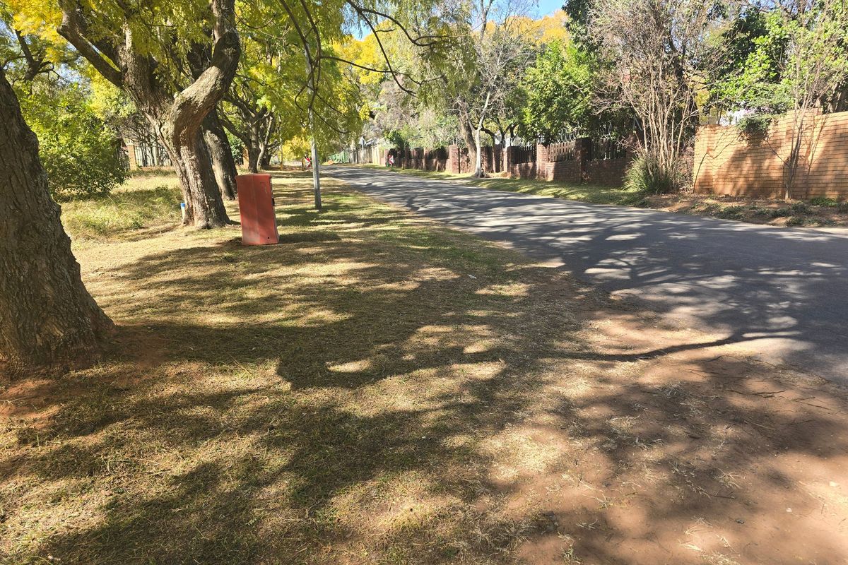 A view of the street frontage featuring mature trees, an asphalt road, and a brick boundary wall along the property perimeter.